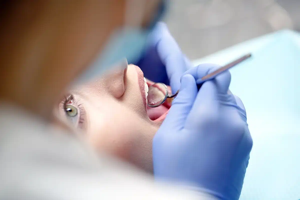Dentist examining a patient’s teeth Clinician wearing gloves examining a patient’s open mouth with a dental mirror, representing professional oral care
