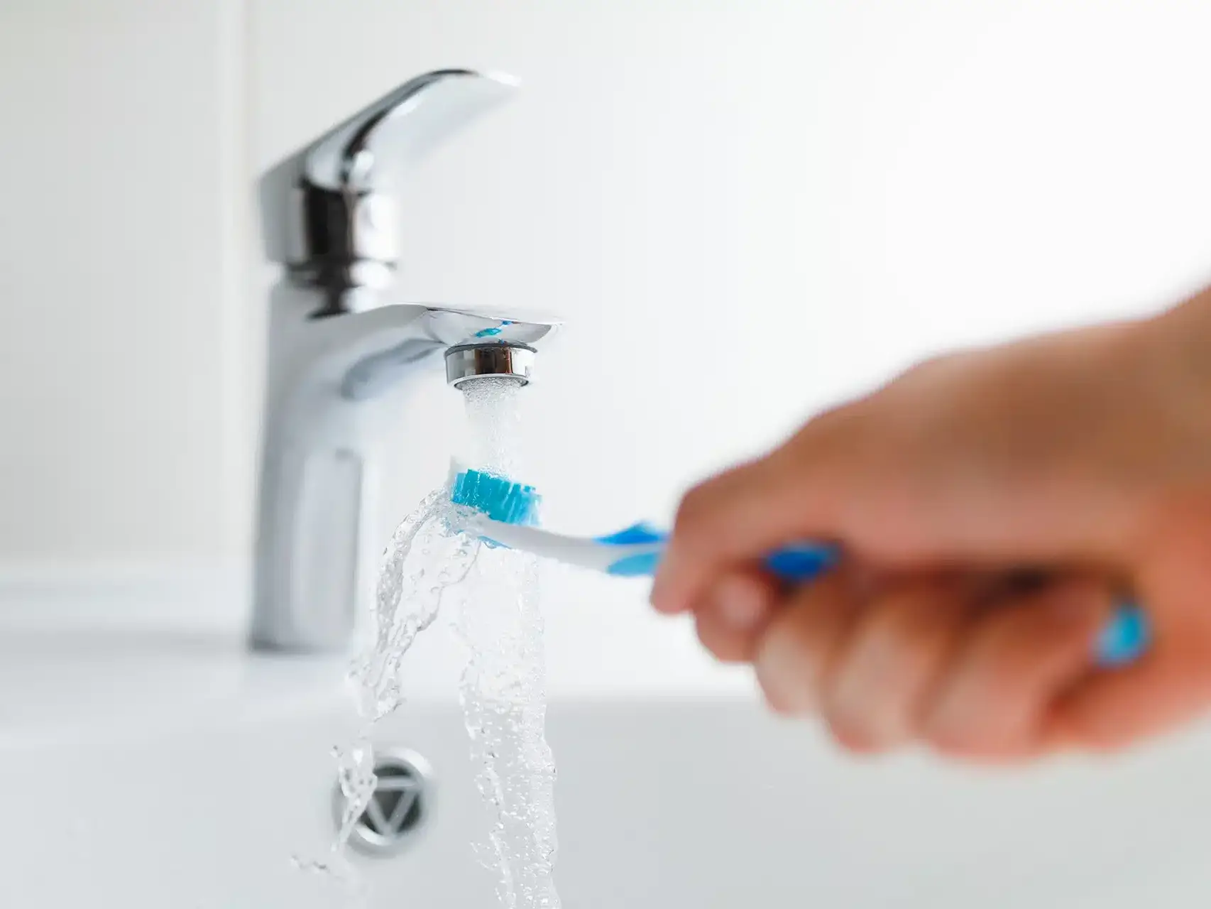 Close-up of a hand placing a toothbrush into a holder next to a bathroom sink, representing everyday brushing habits