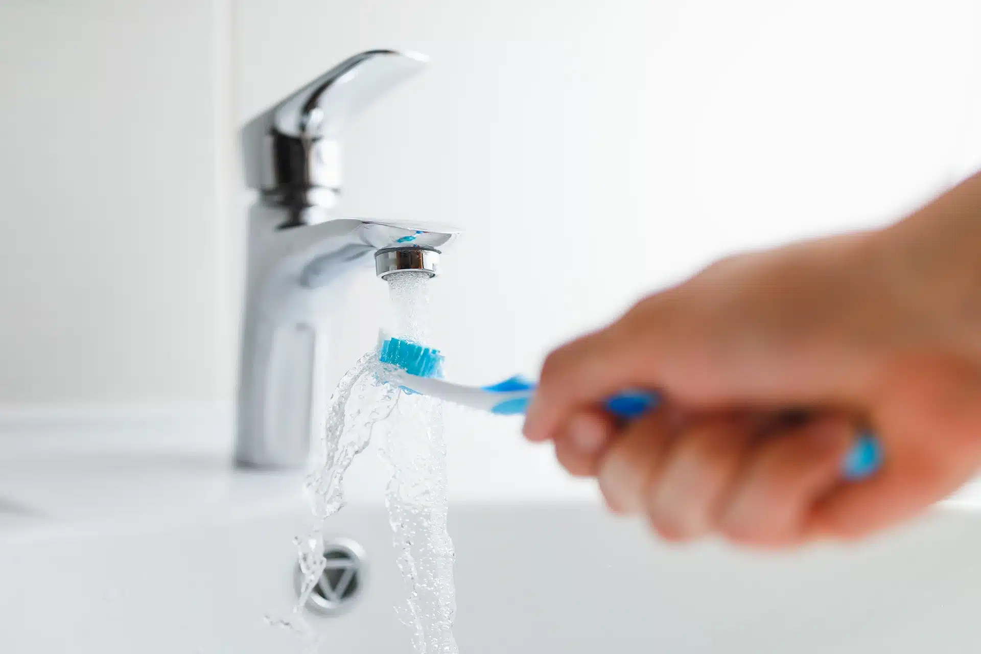 Close-up of a hand placing a toothbrush into a holder next to a bathroom sink, representing everyday brushing habits